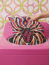 Square psychedelic folk art throw pillow cover printed to look like textured embroidery on a cream background. A large black spider with coral red and magenta markings on its legs and abdomen sits at the center, surrounded by rippling waves in blue violet, coral red, magenta, and golden yellow. Smooth flat 2D print, not raised stitching. Retro gothic Halloween maximalist decor for a sofa, armchair, or goth bedroom, made for spooky season.