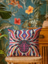 Square psychedelic folk art throw pillow cover printed to look like textured embroidery on a cream background. A large black spider with coral red and magenta markings on its legs and abdomen sits at the center, surrounded by rippling waves in blue violet, coral red, magenta, and golden yellow. Smooth flat 2D print, not raised stitching. Retro gothic Halloween maximalist decor for a sofa, armchair, or goth bedroom, made for spooky season.