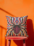 Square psychedelic folk art throw pillow cover printed to look like textured embroidery on a cream background. A large black spider with coral red and magenta markings on its legs and abdomen sits at the center, surrounded by rippling waves in blue violet, coral red, magenta, and golden yellow. Smooth flat 2D print, not raised stitching. Retro gothic Halloween maximalist decor for a sofa, armchair, or goth bedroom, made for spooky season.