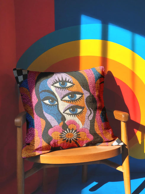Square psychedelic throw pillow cover with a surreal weirdcore face printed to look like textured crewel embroidery. The face has a third eye and extra blue eyes, long dark hair, and a large pink and orange flower over the mouth, framed by radiating wavy stripes in hot pink, orange, and cobalt blue with black and white checkerboard corners. Smooth flat 2D print, not raised stitching. Maximalist 70s trippy decor for a sofa, armchair, or dorm bed.