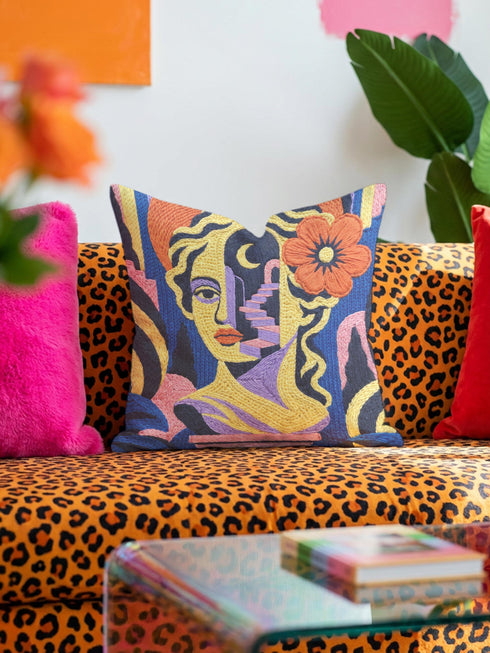 Square eclectic throw pillow cover with a surreal modern art portrait printed to look like textured crewel embroidery on a cobalt blue background. A yellow and purple half face with red lips holds a yellow crescent moon and a pink and purple staircase inside its dark silhouette, with a large orange flower in wavy yellow hair and abstract pink and yellow shapes around it. Smooth flat 2D print, not raised stitching. Maximalist art decor for a sofa, studio chair, or dorm.