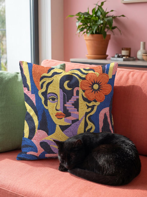 Square eclectic throw pillow cover with a surreal modern art portrait printed to look like textured crewel embroidery on a cobalt blue background. A yellow and purple half face with red lips holds a yellow crescent moon and a pink and purple staircase inside its dark silhouette, with a large orange flower in wavy yellow hair and abstract pink and yellow shapes around it. Smooth flat 2D print, not raised stitching. Maximalist art decor for a sofa, studio chair, or dorm.