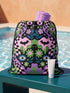 Drawstring backpack measuring 15 by 17 inches, made of 100% polyester with narrow shoulder straps and a drawstring closure. A symmetrical pastel goth print of bats, stylized eyes, flowers, and stars in a soft pastel palette sits on a black base, framed by purple and green checkerboard bands. Creepy cute, whimsigoth, kawaii goth style bag made for the gym, concerts, festivals, travel, school, and everyday carry.