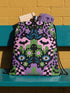 Drawstring backpack measuring 15 by 17 inches, made of 100% polyester with narrow shoulder straps and a drawstring closure. A symmetrical pastel goth print of bats, stylized eyes, flowers, and stars in a soft pastel palette sits on a black base, framed by purple and green checkerboard bands. Creepy cute, whimsigoth, kawaii goth style bag made for the gym, concerts, festivals, travel, school, and everyday carry.