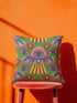 Square weirdcore throw pillow cover printed to look like textured crewel embroidery on a green background. A pink and blue flying saucer with one large blue eye at its center hovers among floating blue eyeballs and red hearts. Smooth flat 2D print, not raised stitching. Maximalist, trippy sci-fi dopamine decor with quirky alien charm for a sofa, dorm bed, gaming chair, or reading nook, made for space lovers and sci-fi fans.