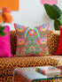 Square folk art throw pillow cover printed to look like textured crewel embroidery on a coral orange background. A green frog sits cross-legged in a meditation pose beneath a blue and yellow arch, surrounded by symmetrical pink flowers. Smooth flat 2D print, not raised stitching. Colorful, whimsical, maximalist dopamine decor for a yoga room, meditation corner, sofa, or reading nook, made for yoga lovers and frog fans.