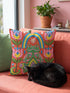 Square folk art throw pillow cover printed to look like textured crewel embroidery on a coral orange background. A green frog sits cross-legged in a meditation pose beneath a blue and yellow arch, surrounded by symmetrical pink flowers. Smooth flat 2D print, not raised stitching. Colorful, whimsical, maximalist dopamine decor for a yoga room, meditation corner, sofa, or reading nook, made for yoga lovers and frog fans.
