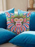 Square folk art throw pillow cover printed to look like thick crewel yarn embroidery. A bold, whimsical monkey face in olive green and pink stares out with intense yellow eyes, framed by a retro scalloped floral collar. Smooth flat 2D print, not raised stitching. Clowncore, junglecore, and weirdcore maximalist decor with eclectic, quirky charm for a sofa, accent chair, or bedroom, made for animal lovers and alt renters.