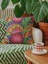 Square maximalist throw pillow cover printed to look like bold crewel embroidery on a solid royal blue background. Tacos with green, red, and brown fillings scatter across the design with bright green saguaro cacti, large pink and red starburst flowers, and small yellow stars. Smooth flat 2D print, not raised stitching. Colorful, quirky dopamine decor for a sofa, kitchen bench, or breakfast nook, made for taco lovers and foodies.