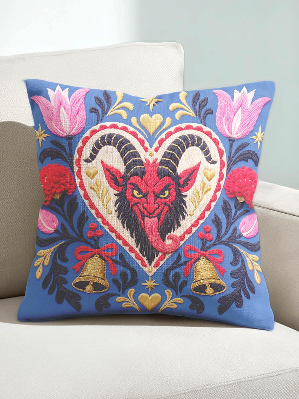 Square gothic Christmas throw pillow cover in a folk art design printed to look like textured crewel embroidery on a medium blue background. A red horned Krampus face with a long tongue sits inside a white and gold scalloped heart, surrounded by dark leafy vines, pink tulips, red carnations, gold bells tied with red bows, and small gold stars. Smooth flat 2D print, not raised stitching. Maximalist spooky holiday decor for a sofa, armchair, or goth bedroom.
