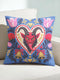 Square gothic Christmas throw pillow cover in a folk art design printed to look like textured crewel embroidery on a medium blue background. A red horned Krampus face with a long tongue sits inside a white and gold scalloped heart, surrounded by dark leafy vines, pink tulips, red carnations, gold bells tied with red bows, and small gold stars. Smooth flat 2D print, not raised stitching. Maximalist spooky holiday decor for a sofa, armchair, or goth bedroom.