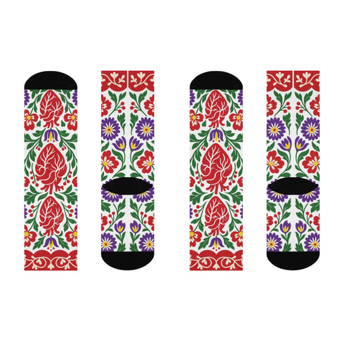 Pair of crew length socks with an all-over folk art print on a cream background. Red anatomical hearts stack vertically between symmetrical floral sprays with fine cream vessel lines, curling green stems and leaves, red flowers, purple tulip-shaped blooms, and small yellow accents. Red cuffs carry cream scrolling vines and small hearts above a scalloped border. Reinforced black heel and toe, striped ribbed cuff. Maximalist medical gift socks.