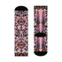 Pair of crew length socks with an all-over pastel goth print on a pastel pink background. Black-outlined human skulls with small orange eyes on their foreheads, all-seeing eyes with orange rays, crescent moons, curling leaves, and pink diamond stars sit in a symmetrical dark damask layout. Black cuff with a scalloped edge, orange flames, and pink flourishes. Reinforced black heel and toe, striped ribbed cuff. Western goth tattoo flash style.