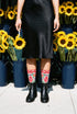 Pair of crew length socks with an all-over folk art print on a cream background. Red anatomical hearts stack vertically between symmetrical floral sprays with fine cream vessel lines, curling green stems and leaves, red flowers, purple tulip-shaped blooms, and small yellow accents. Red cuffs carry cream scrolling vines and small hearts above a scalloped border. Reinforced black heel and toe, striped ribbed cuff. Maximalist medical gift socks.