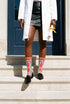 Pair of crew length socks with an all-over folk art print on a cream background. Red anatomical hearts stack vertically between symmetrical floral sprays with fine cream vessel lines, curling green stems and leaves, red flowers, purple tulip-shaped blooms, and small yellow accents. Red cuffs carry cream scrolling vines and small hearts above a scalloped border. Reinforced black heel and toe, striped ribbed cuff. Maximalist medical gift socks.