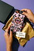 Pair of crew length socks with an all-over pastel goth print on a pastel pink background. Black-outlined human skulls with small orange eyes on their foreheads, all-seeing eyes with orange rays, crescent moons, curling leaves, and pink diamond stars sit in a symmetrical dark damask layout. Black cuff with a scalloped edge, orange flames, and pink flourishes. Reinforced black heel and toe, striped ribbed cuff. Western goth tattoo flash style.