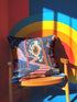 Square surreal liminal space throw pillow cover printed to look like textured embroidery on a dark navy background. A giant blue and white eyeball planet with an orange iris glows inside pink stone arches above a pink and white striped staircase curving over dark blue water, with lavender clouds, blue aqueduct arches, and orange potted palms. Smooth flat 2D print, not raised stitching. Psychedelic dreamscape decor for a sofa, bedroom chair, or reading nook.