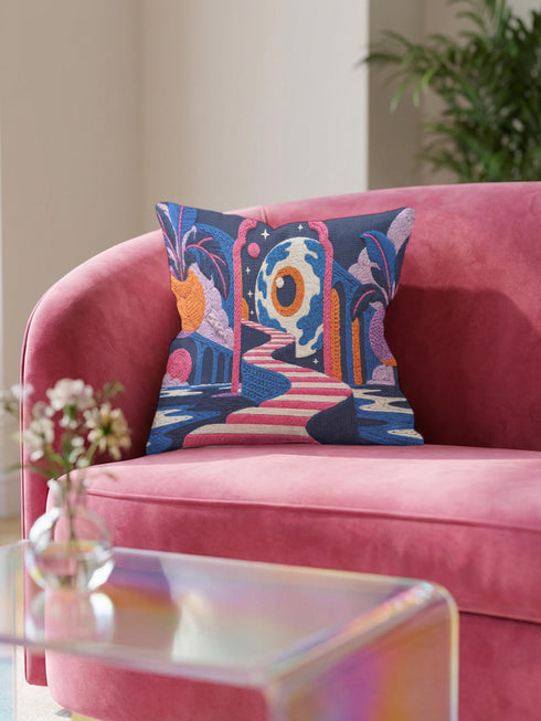 Square surreal liminal space throw pillow cover printed to look like textured embroidery on a dark navy background. A giant blue and white eyeball planet with an orange iris glows inside pink stone arches above a pink and white striped staircase curving over dark blue water, with lavender clouds, blue aqueduct arches, and orange potted palms. Smooth flat 2D print, not raised stitching. Psychedelic dreamscape decor for a sofa, bedroom chair, or reading nook.
