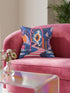 Square surreal liminal space throw pillow cover printed to look like textured embroidery on a dark navy background. A giant blue and white eyeball planet with an orange iris glows inside pink stone arches above a pink and white striped staircase curving over dark blue water, with lavender clouds, blue aqueduct arches, and orange potted palms. Smooth flat 2D print, not raised stitching. Psychedelic dreamscape decor for a sofa, bedroom chair, or reading nook.