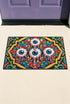 Rectangular doormat with a black background and black edge trim, printed in a flat 2D faux embroidery style. A golden yellow stepped octagon frames four large bloodshot eyeballs with blue irises and dripping pink, with two small peeking eyes among the florals. Hot pink, orange, turquoise, and green folk art petals and green vines fill the corners. Polyester surface with a low pile and non-slip rubber backing. Psychedelic 70s creepy cute decor.