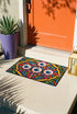 Rectangular doormat with a black background and black edge trim, printed in a flat 2D faux embroidery style. A golden yellow stepped octagon frames four large bloodshot eyeballs with blue irises and dripping pink, with two small peeking eyes among the florals. Hot pink, orange, turquoise, and green folk art petals and green vines fill the corners. Polyester surface with a low pile and non-slip rubber backing. Psychedelic 70s creepy cute decor.