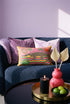 Rectangular 20 by 12 inch lumbar pillow cover with a folk art alligator design printed to look like heavy crewel embroidery on a bright pink background. A large grey and yellow alligator lounges above red, teal, and yellow wavy water lines, flanked by two green palm trees, a pink and yellow sunburst, a red sun, and a green tropical plant. Smooth flat 2D print, not raised stitching. Tropical maximalist decor for a bed, sofa, or reading nook.