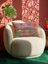 Rectangular 20 by 12 inch lumbar pillow cover with a folk art alligator design printed to look like heavy crewel embroidery on a bright pink background. A large grey and yellow alligator lounges above red, teal, and yellow wavy water lines, flanked by two green palm trees, a pink and yellow sunburst, a red sun, and a green tropical plant. Smooth flat 2D print, not raised stitching. Tropical maximalist decor for a bed, sofa, or reading nook.