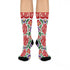 Pair of crew length socks with an all-over folk art print on a cream background. Red anatomical hearts stack vertically between symmetrical floral sprays with fine cream vessel lines, curling green stems and leaves, red flowers, purple tulip-shaped blooms, and small yellow accents. Red cuffs carry cream scrolling vines and small hearts above a scalloped border. Reinforced black heel and toe, striped ribbed cuff. Maximalist medical gift socks.