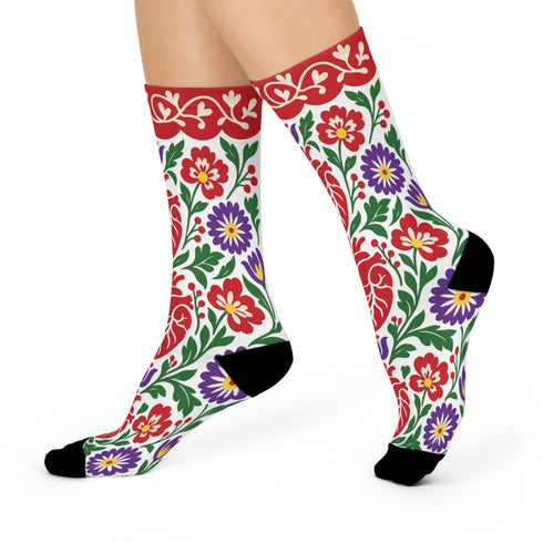 Pair of crew length socks with an all-over folk art print on a cream background. Red anatomical hearts stack vertically between symmetrical floral sprays with fine cream vessel lines, curling green stems and leaves, red flowers, purple tulip-shaped blooms, and small yellow accents. Red cuffs carry cream scrolling vines and small hearts above a scalloped border. Reinforced black heel and toe, striped ribbed cuff. Maximalist medical gift socks.