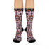 Pair of crew length socks with an all-over pastel goth print on a pastel pink background. Black-outlined human skulls with small orange eyes on their foreheads, all-seeing eyes with orange rays, crescent moons, curling leaves, and pink diamond stars sit in a symmetrical dark damask layout. Black cuff with a scalloped edge, orange flames, and pink flourishes. Reinforced black heel and toe, striped ribbed cuff. Western goth tattoo flash style.