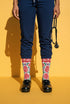 Pair of crew length socks with an all-over folk art print on a cream background. Red anatomical hearts stack vertically between symmetrical floral sprays with fine cream vessel lines, curling green stems and leaves, red flowers, purple tulip-shaped blooms, and small yellow accents. Red cuffs carry cream scrolling vines and small hearts above a scalloped border. Reinforced black heel and toe, striped ribbed cuff. Maximalist medical gift socks.