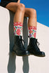 Pair of crew length socks with an all-over folk art print on a cream background. Red anatomical hearts stack vertically between symmetrical floral sprays with fine cream vessel lines, curling green stems and leaves, red flowers, purple tulip-shaped blooms, and small yellow accents. Red cuffs carry cream scrolling vines and small hearts above a scalloped border. Reinforced black heel and toe, striped ribbed cuff. Maximalist medical gift socks.