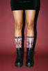 Pair of crew length socks with an all-over pastel goth print on a pastel pink background. Black-outlined human skulls with small orange eyes on their foreheads, all-seeing eyes with orange rays, crescent moons, curling leaves, and pink diamond stars sit in a symmetrical dark damask layout. Black cuff with a scalloped edge, orange flames, and pink flourishes. Reinforced black heel and toe, striped ribbed cuff. Western goth tattoo flash style.