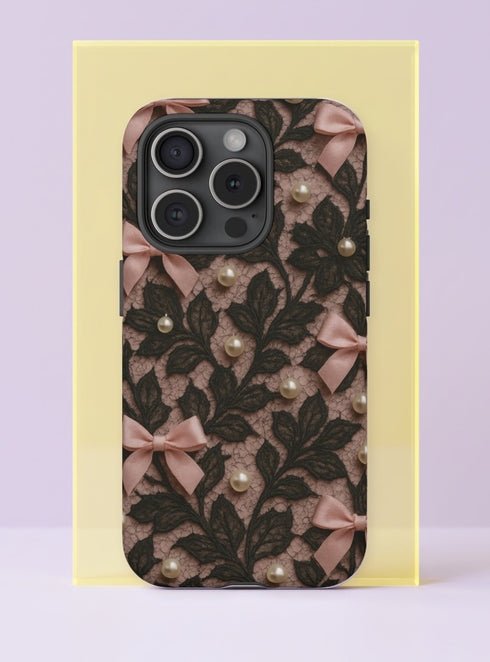 Front view of a dual layer tough phone case printed edge to edge with a coquette lace design. Black floral lace vines climb over a blush nude background, decorated with little pink satin bows and scattered cream pearls, all rendered as a realistic flat print. It looks like vintage lingerie and a jewelry box had a very pretty argument. Dark coquette lace and pearls phone accessory with open ports and a precise camera cutout.