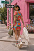 Short sleeve crew neck t-shirt dress on a cream background with an allover retro mod flower medallion print. Bold 60s daisies in red, yellow, and white sit at the center of concentric rainbow rings in lime green, hot pink, orange, and royal blue, with small magenta squares and tiny red checkerboard accents between the motifs. Above-the-knee straight fit silhouette in a 95 percent cotton, 5 percent elastane heavyweight stretch blend. Groovy retro flower power dress for dopamine dressing and easy summer outfi