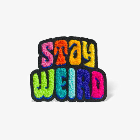 Colorful patch with the phrase 'Stay Weird' in vibrant, multicolored, textured letters, set against a black background. The design is playful and bold, celebrating uniqueness and individuality.