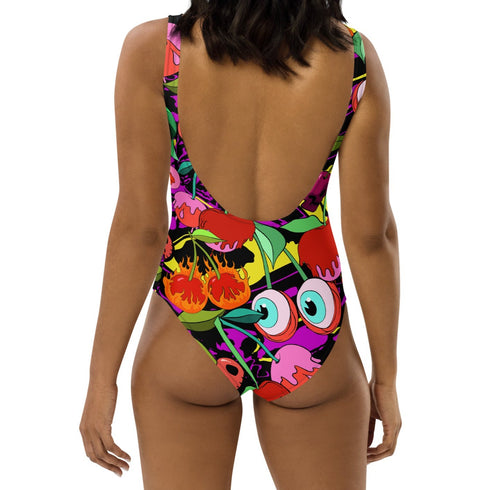 A colorful one-piece swimsuit features a vibrant, quirky pattern with cherries, cartoon eyes, and playful designs on a dark background.