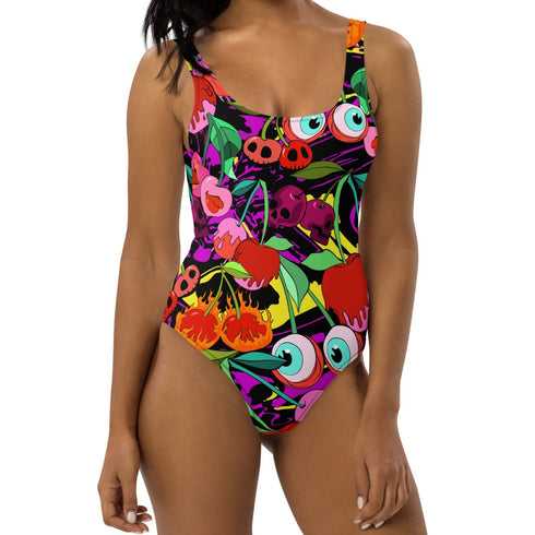 A colorful one-piece swimsuit features a vibrant, quirky pattern with cherries, cartoon eyes, and playful designs on a dark background.