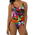 A colorful one-piece swimsuit features a vibrant, quirky pattern with cherries, cartoon eyes, and playful designs on a dark background.