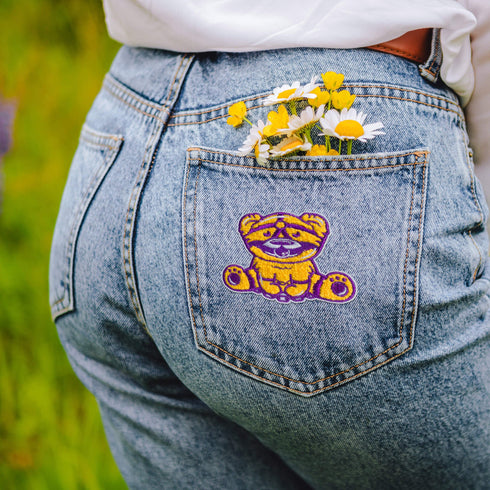 Patch featuring a cute bear in yellow and purple with a playful expression, wearing a BDSM harness and a ball gag. The design is fun and whimsical, combining bold colors with a cheeky style.