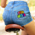 Colorful patch with the phrase 'Stay Weird' in vibrant, multicolored, textured letters, set against a black background. The design is playful and bold, celebrating uniqueness and individuality.