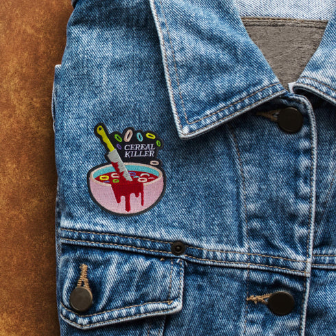 Patch featuring a bowl of cereal with a dripping knife and the text 'Cereal Killer,' set against a light pink background. The design combines playful cereal elements with a humorous, spooky twist.