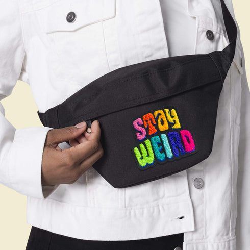 Colorful patch with the phrase 'Stay Weird' in vibrant, multicolored, textured letters, set against a black background. The design is playful and bold, celebrating uniqueness and individuality.