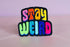 Colorful patch with the phrase 'Stay Weird' in vibrant, multicolored, textured letters, set against a black background. The design is playful and bold, celebrating uniqueness and individuality.
