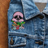 Patch featuring a pink skull biting into colorful vegetables with the word 'VEGAN' in bold letters below, set against a black background. The design is vibrant and edgy, blending vegan pride with a punk rock aesthetic.