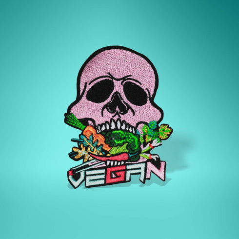 Patch featuring a pink skull biting into colorful vegetables with the word 'VEGAN' in bold letters below, set against a black background. The design is vibrant and edgy, blending vegan pride with a punk rock aesthetic.