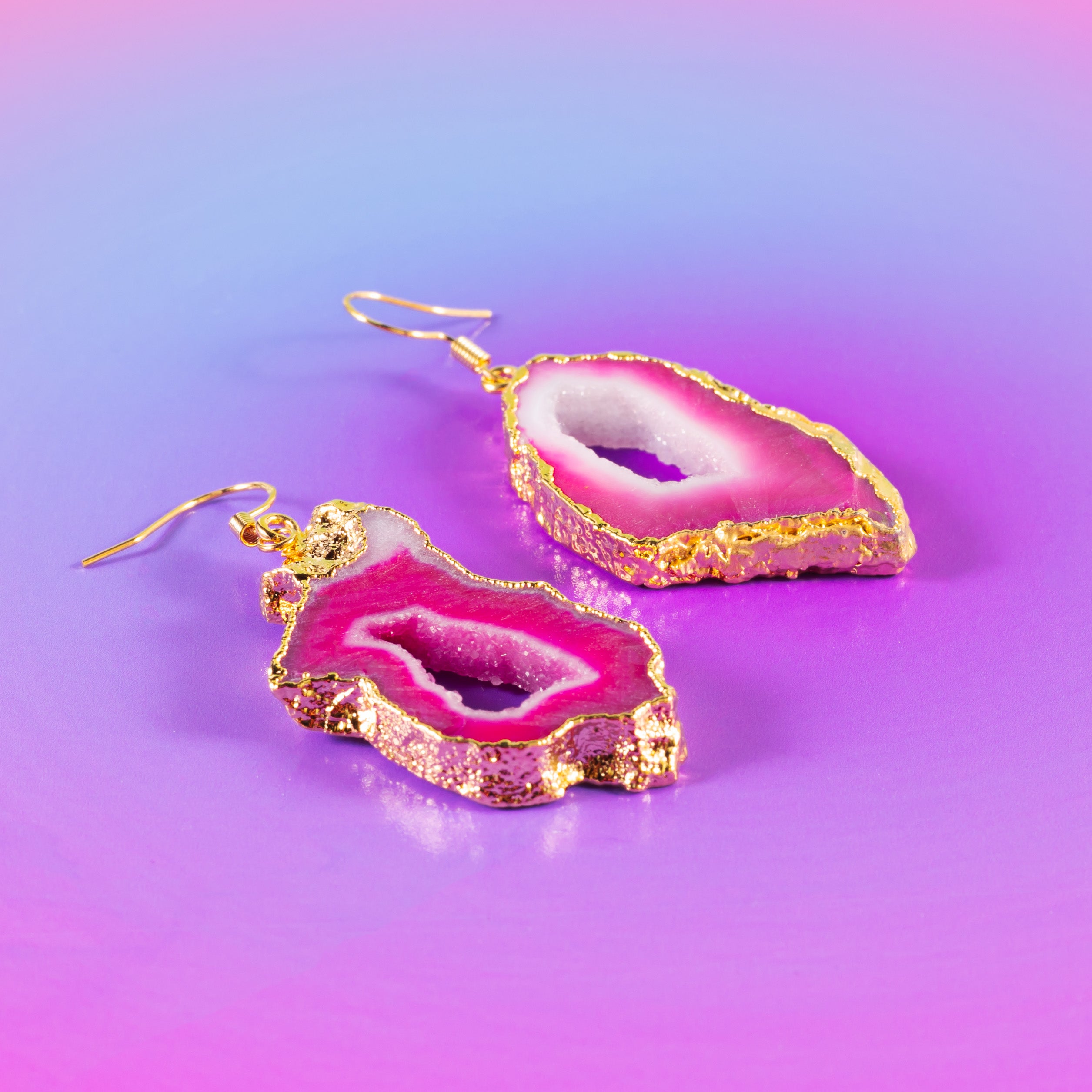a pair of pink and gold earrings on a purple background