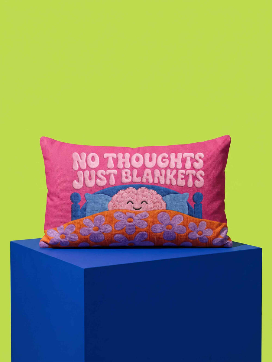 A bright magenta pink rectangular lumbar pillow cover featuring a flat 2D printed faux embroidery design. The printed illusion shows light pink bubble text reading NO THOUGHTS JUST BLANKETS. Below the text is a cartoon pink brain with a happy face, tucked into a blue bed with blue pillows. The brain is covered by a textured-looking orange blanket decorated with light purple daisies. The entire design is a smooth printed trompe l'oeil stitch effect, not real woven or stitched texture.
