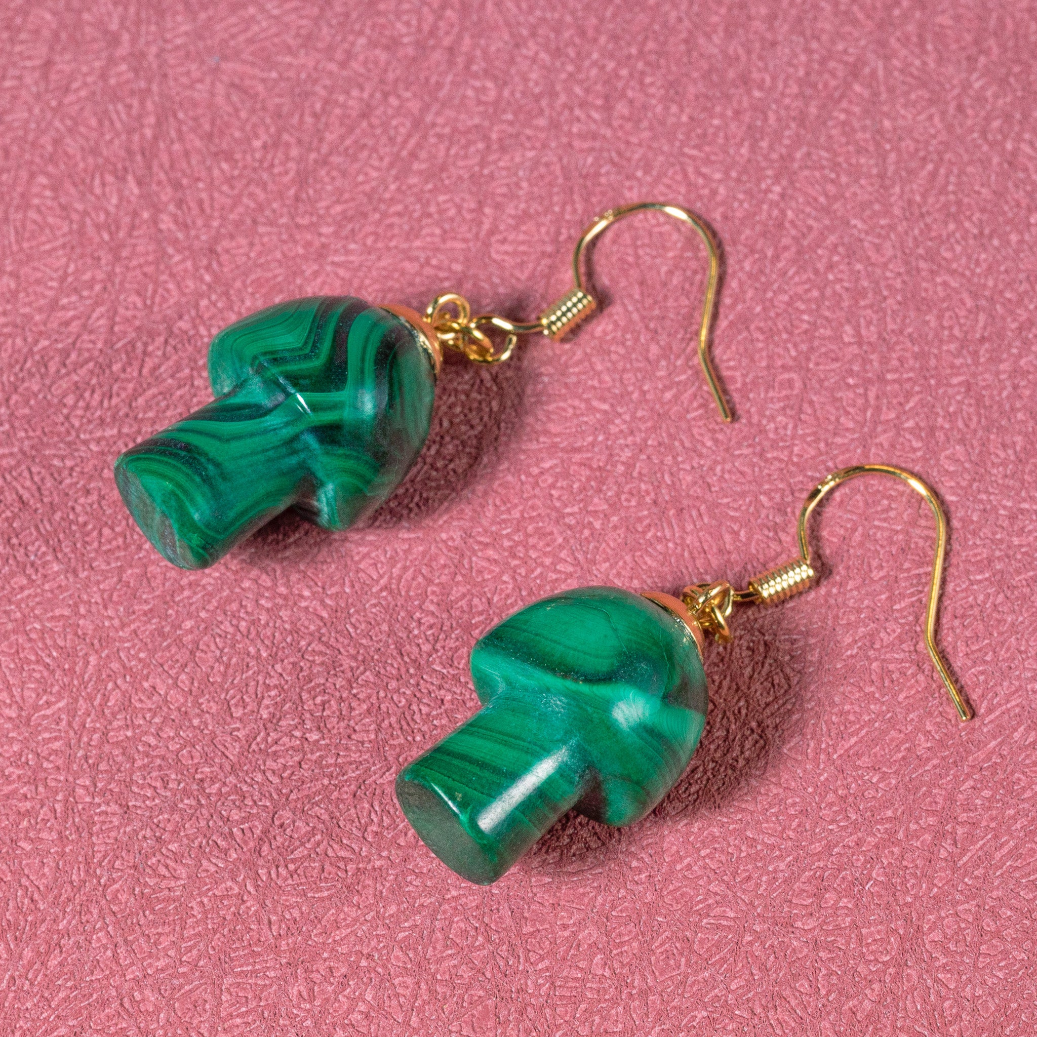 a pair of green earrings sitting on top of a pink surface
