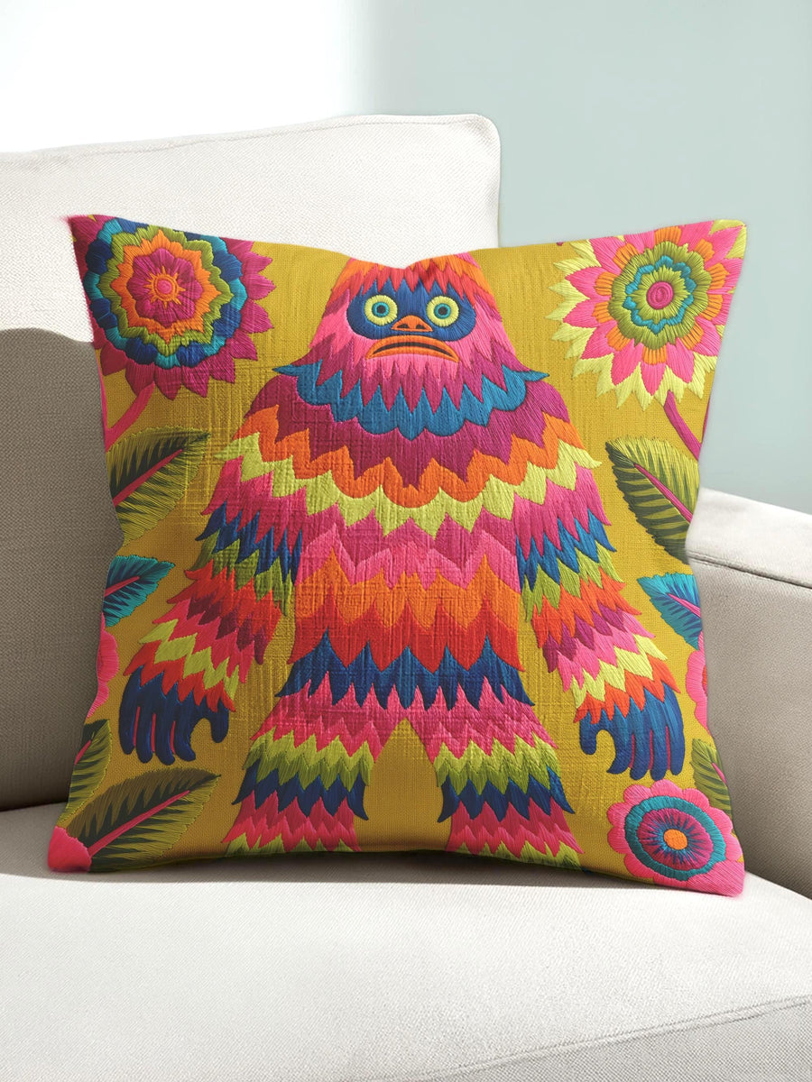 A square faux embroidery pillow featuring a brightly colored maximalist design against a mustard yellow background. In the center stands a stylized, furry Bigfoot or Sasquatch figure rendered in vibrant layers of pink, orange, blue, and lime green with a blue face and yellow eyes. The central creature is surrounded by large, detailed symmetrical pink and blue flowers and leaves. The flat printed fabric creates a highly realistic optical illusion of dimensional crewel embroidery stitches.